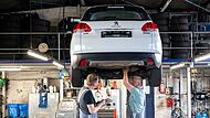 zwei Mechaniker arbeiten in einer Kfz-Werkstatt an einem Auto