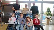 Die ersten K&auml;sten brachte Rewe-Marktleiter Dominik Bachmeier (hinten links) gleich mit in die Wiesentheider Schule. &Uuml;ber die gespendeten Getr&auml;nke f&uuml;r die Mittagsbetreuung freuten sich neben den Sch&uuml;lern auch  Christine Zwillich-St&ouml;cker von der Mittagsbetreuung und Wiesentheids B&uuml;rgermeister Klaus K&ouml;hler.
