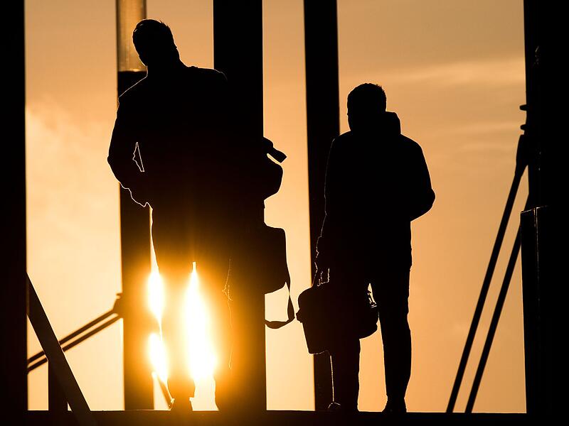 Zwei Männer gehen mit Aktentasche bei Sonnenaufgang über Brücke Zwei Männer gehen mit Aktentasche bei Sonnenaufgang über Brücke
