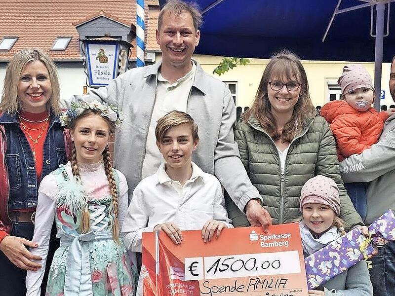 Scheck&uuml;bergabe mit (v. l.) Verena Eichfelder von Kachelofen-Premiumpartner Kaufhaus Schrill, ihren beiden Kindern Greta und Gabriel, Sebastian Linz, Amilias Mutter Sonja, Amilias Schwester Mathilda, Amilia und ihrem Vater Michael.