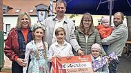 Scheck&uuml;bergabe mit (v. l.) Verena Eichfelder von Kachelofen-Premiumpartner Kaufhaus Schrill, ihren beiden Kindern Greta und Gabriel, Sebastian Linz, Amilias Mutter Sonja, Amilias Schwester Mathilda, Amilia und ihrem Vater Michael.