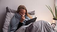 Eine Frau mit Tablet liegt krank im Bett