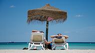 Touristen liegen am Strand unter einem Sonnenschirm