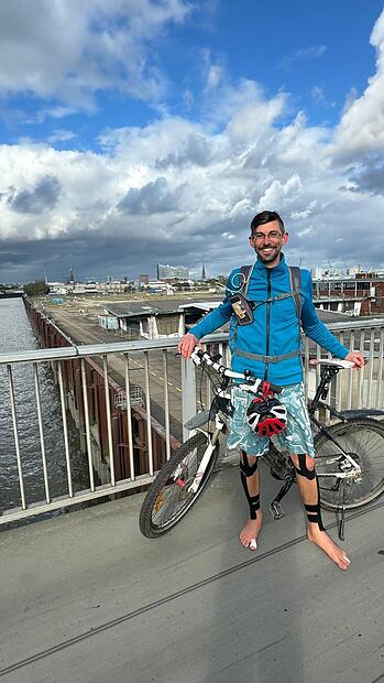 Melf Hauck glücklich und und erleichtert am Ziel am Hamburger Hafen, barfuß und mit Fahrrad.