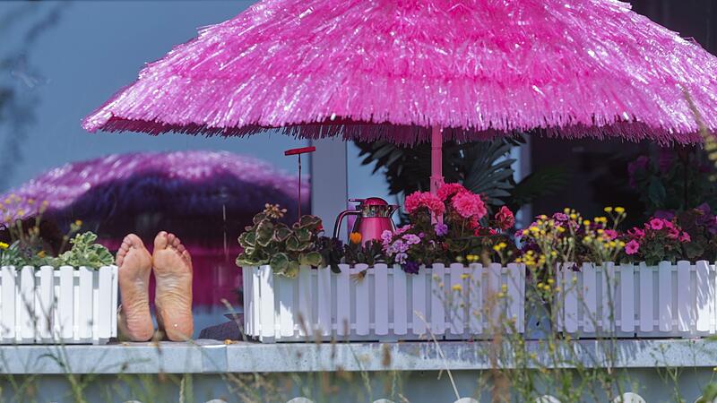 Frau liegt auf einem Balkon unter einem pinken Sonnenschirm
