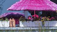 Frau liegt auf einem Balkon unter einem pinken Sonnenschirm
