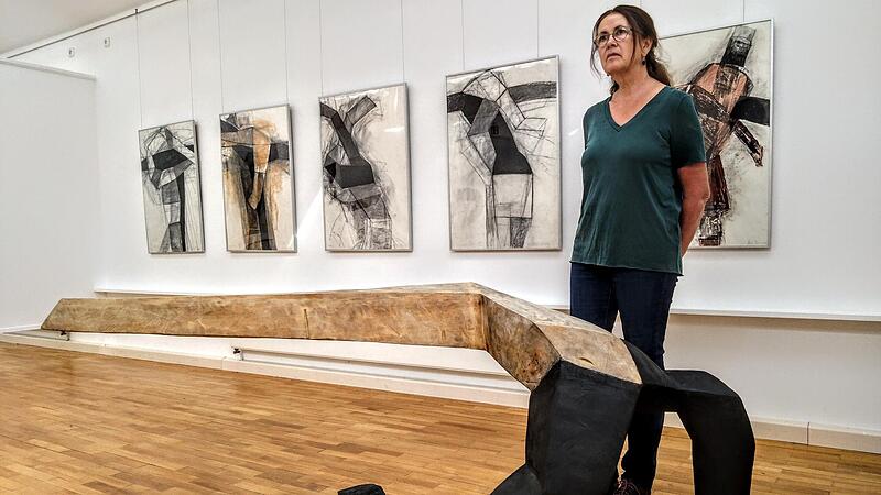Beate Debus neben ihrer Skulptur &bdquo;Aushalten&ldquo; aus Pappelholz, im Hintergrund Zeichnungen, die als Vorlage f&uuml;r weitere Skulpturen dienten.