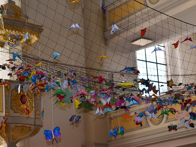 Vesperkirche 2026: Der Kirchenhimmel von St. Moriz h&auml;ngt voller bunter Schmetterlinge der Hoffnung.