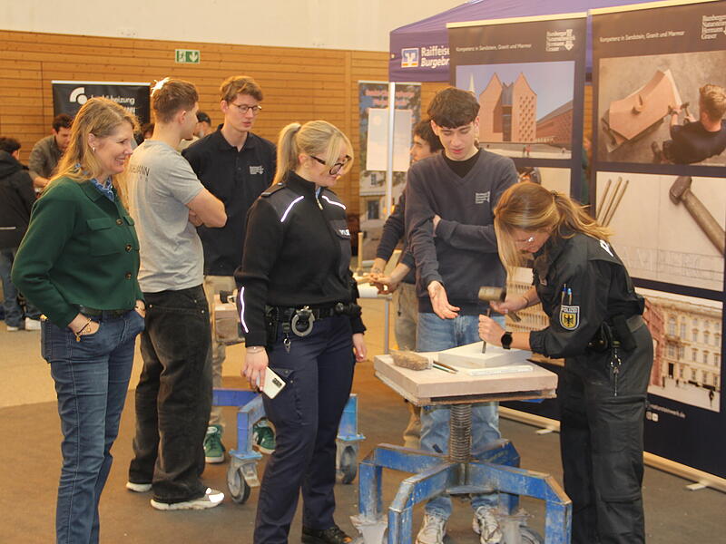 Zwei Polizistinnen versuchen sich am Stand des Bamberger Natursteinwerk Graser an der Steinbearbeitung.