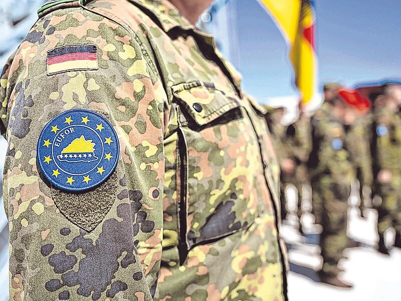 Ein Offizier mit dem &bdquo;Eufor&ldquo;-Zeichen steht vor einer deutschen Flagge im Camp Butmir.