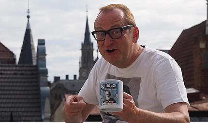 Unser Bild zeigt Volker Hei&szlig;mann mit seinem Gastgeschenk und der Kulisse von Bad Kissingen im Hintergrund.