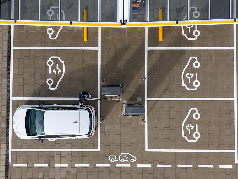 Ein Mann steht auf einem Ladepark in Sachsen und steckt ein Ladekabel in den Tankstutzen seines Elektroautos (Aufnahme mit einer Drohne).