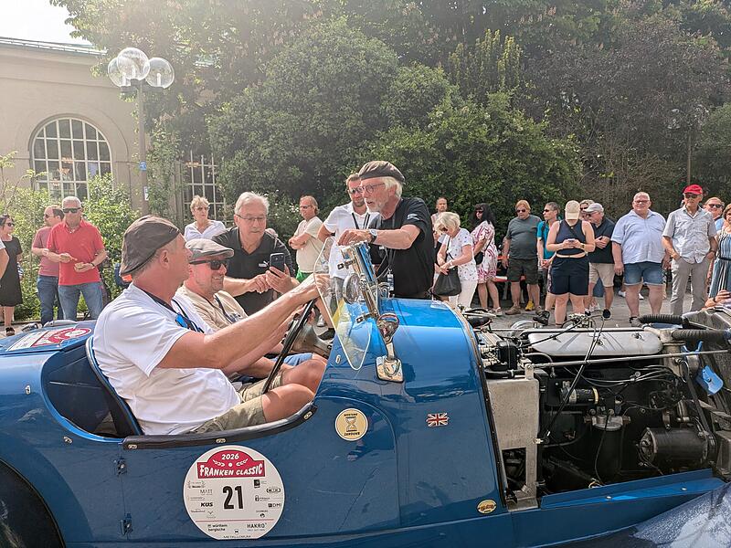 Ein blauer Vorkriegs-Sportwagen rollt beim Zieleinlauf der Franken Classic 2026 ins Ziel, umringt von neugierigen Zuschauern.Franken Classic 2026 Ein blauer Vorkriegs-Sportwagen rollt beim Zieleinlauf der Franken Classic 2026 ins Ziel, umringt von neugierigen Zuschauern.