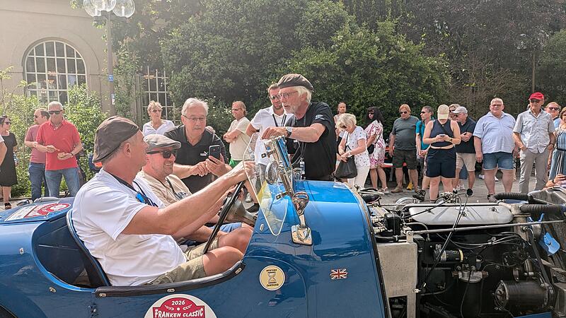 Ein blauer Vorkriegs-Sportwagen rollt beim Zieleinlauf der Franken Classic 2026 ins Ziel, umringt von neugierigen Zuschauern.