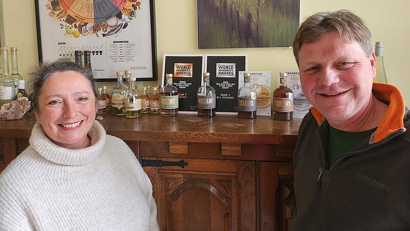 Kathrin Kilian und ihr Mann Michael stehen vor dem Regal, auf dem die ausgezeichneten Whiskys angeordnet sind.