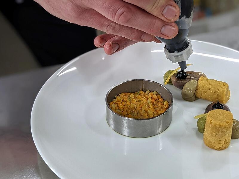 Die Kichererbsenkroketten kommen auf den Teller. Neben der Schwarzen Knoblauch-Creme ist hier noch eine Petersiliencreme und ein Erbsenmiso zu sehen.