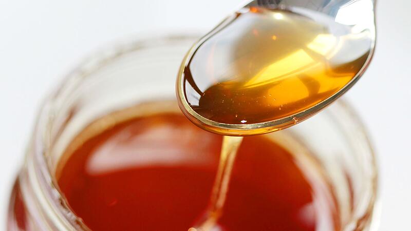 Honig flie&szlig;t von einem L&ouml;ffel zur&uuml;ck ins Honigglas