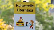 Ein Schild mit der Aufschrift „Haltestelle Elterntaxi“ steht vor einer Dresdner Grundschule.