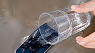 Wasser aus einem Glas ergießt sich über ein iPhone.