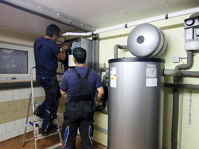 Zwei Handwerker  stellen eine gerade installierte W&auml;rmepumpe im Keller einer Doppelhaush&auml;lfte ein. Das Geb&auml;udemodernisierungsgesetz erlaubt jetzt allerdings auch den l&auml;ngeren Betrieb von Gas- oder &Ouml;lheizungen.