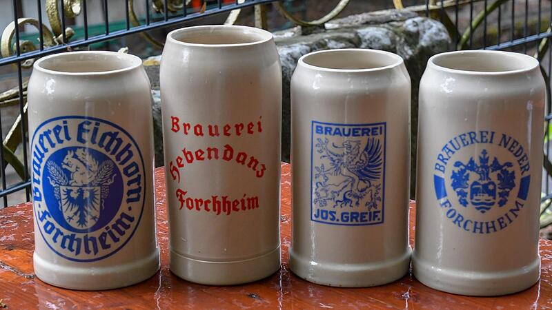 Vier Maßkrüge mit den Namen und Wappen der Brauereien in der Stadt Forchheim stehen auf einem Biertisch.Forchheim & Fränkische Schweiz