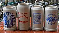 Vier Maßkrüge mit den Namen und Wappen der Brauereien in der Stadt Forchheim stehen auf einem Biertisch.Forchheim & Fränkische Schweiz