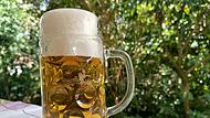 0,5-Liter-Glaskrug auf einem Gartentisch, gef&uuml;llt mit alkoholfreiem hellen Bier.