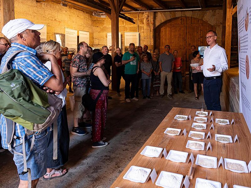 Andreas Hubmann (r.) stellt Besuchern das neu er&ouml;ffnete Scheunenmuseum der Minderleinsm&uuml;hle vor. Die Ausstellung zeigt historische Dokumente vom traditionellen Handwerksbetrieb zum modernen Bio-Unternehmen.