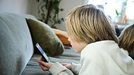 Ein Junge liegt auf einem Sofa und guckt auf sein Smartphone