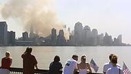 Passanten mit US-Fahnen betrachten am 12. September 2001 von New Jersey aus die in Rauch und Staub gehüllte Skyline von Manhattan. Dort wo am Vortag noch die beiden Türme des World Trade Centers gestanden hatten, ist jetzt nur noch eine Qualmwolke zu sehen.