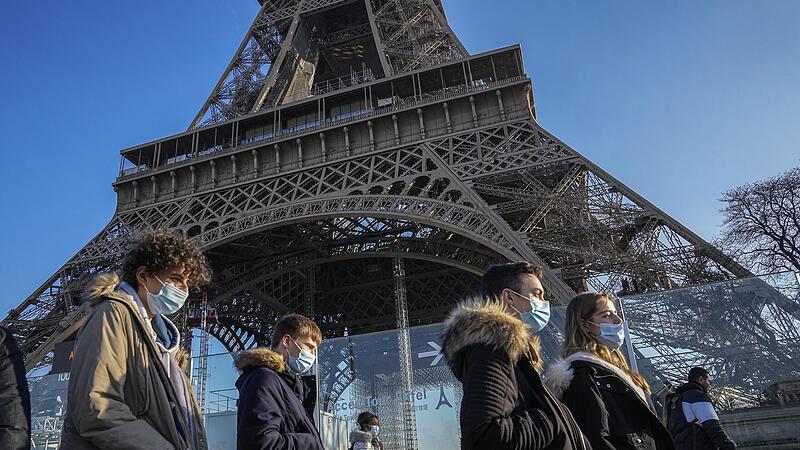 Menschen tragen Schutzmasken und gehen in Paris am Eiffelturm vorbei. Trotz der hohen Infektionszahlen ist die Regierung bem&uuml;ht, die Franzosen m&ouml;glichst wenig einzuschr&auml;nken.