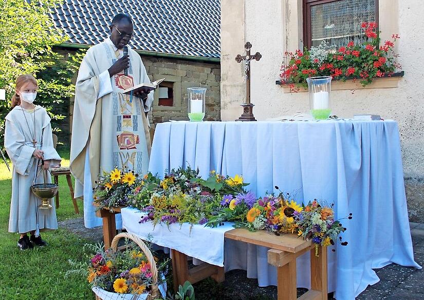 Abbé Pierre spricht das Segensgebet über die farbenprächtigen Kräuterbüschel und besprengt sie mit Weihwasser. Links im Bild Ministrantin Marlene Pfeuffer, dahinter das „Höreder“ Pfarrhaus mit einladendem Blumenschmuck. Abbé Pierre spricht das Segensgebet über die farbenprächtigen Kräuterbüschel und besprengt sie mit Weihwasser. Links im Bild Ministrantin Marlene Pfeuffer, dahinter das „Höreder“ Pfarrhaus mit einladendem Blumenschmuck.