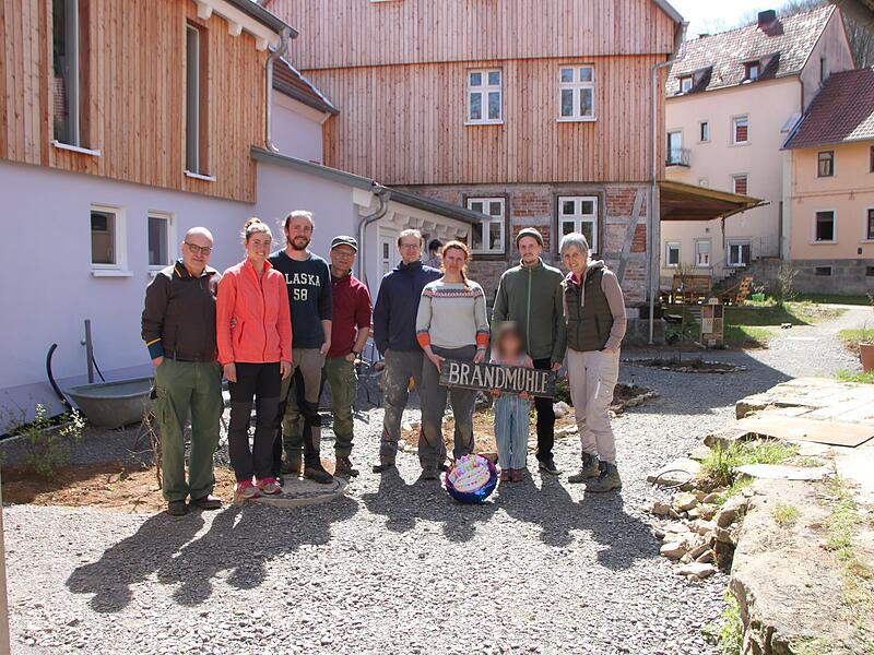 Auf dem Foto von links stehen vor den Wohnh&auml;usern und der M&uuml;hle: Klaus Reichert, Anna Baumgartner, Simon Memmel, Rainer Neubauer, Andr&eacute; und Magdalena Gl&ouml;ckner, Jakob mit Kind sowie Martina Neubauer.