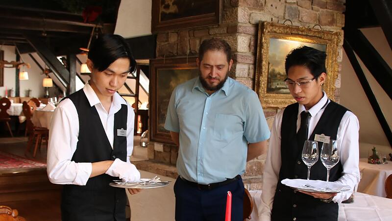 Petko Novakov (Mitte), stellvertretender Leiter des Restaurants im Hotel Neumühle, geht mit den beiden vietnamesischen Auszubildenden Huy Nguyen (links) und Trung Le (rechts) das richtige Decken und Dekorieren eines Tisches durch. Petko Novakov (Mitte), stellvertretender Leiter des Restaurants im Hotel Neumühle, geht mit den beiden vietnamesischen Auszubildenden Huy Nguyen (links) und Trung Le (rechts) das richtige Decken und Dekorieren eines Tisches durch.