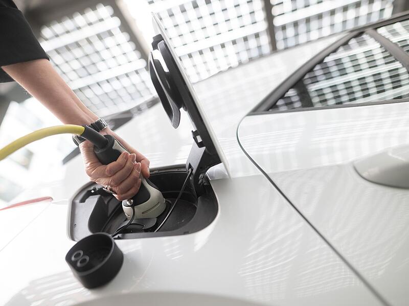 Frau steckt einen Ladestecker für ein E-Auto in eine Buchse Frau steckt einen Ladestecker für ein E-Auto in eine Buchse