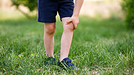 Anonymous Child Scratching Itchy Skin Irritation on Legs After Playing on Green Grass