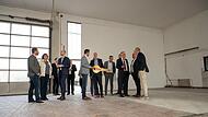 Die Gäste schauen sich in der noch leeren Halle um, in der Mitte mit Schlüssel der Präsident der Hochschule Coburg, Stefan Gast.
