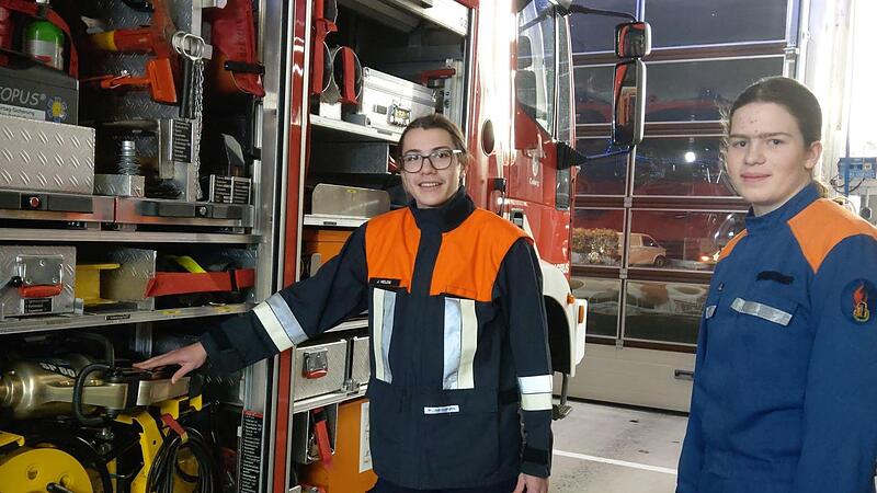 Jakob Heilos (links) und Paul M&uuml;ller am R&uuml;stwagen. Paul M&uuml;ller tr&auml;gt noch den Anzug der Jugendfeuerwehr, Jakob Heilos ist bereits als Feuerwehrmann eingekleidet.