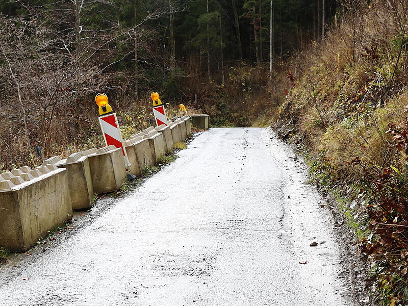 Durch umgestürzte Bäume am Hang ist die Straße (links hinter und unter den Betonquadern) teilweise instabil und die Leitplanke verbogen.