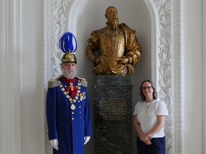 Mirko Keß als Prinzregent Luitpold von Bayern und Maskenbildnerin Annalena Rohnke vor der Büste des Adeligen. Mirko Keß als Prinzregent Luitpold von Bayern und Maskenbildnerin Annalena Rohnke vor der Büste des Adeligen.
