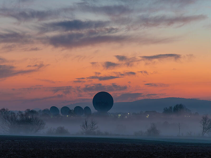 Das Bild zeigt die Erdfunkstelle zur Morgend&auml;mmerung. Auf den Saalewiesen ziehen die Schwaden des Morgennebels und noch ist der Himmel deutlich heller, als die umgebende Landschaft. Durch die Wolkenschleier wirkt auch der Himmel deutlich spannender, als dies bei wolkenlosem Himmel der Fall w&auml;re, meint Ralf Bauer.