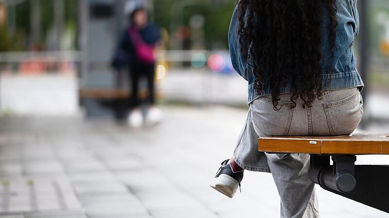 Eine junge Frau sitzt an einer Haltestelle auf einer Bank Eine junge Frau sitzt an einer Haltestelle auf einer Bank