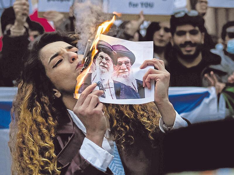Eine Demonstrantin zündet sich ihre Zigarette an einem brennenden Foto des Obersten Führers des Iran, Ali Chamenei, an. Eine Demonstrantin zündet sich ihre Zigarette an einem brennenden Foto des Obersten Führers des Iran, Ali Chamenei, an.