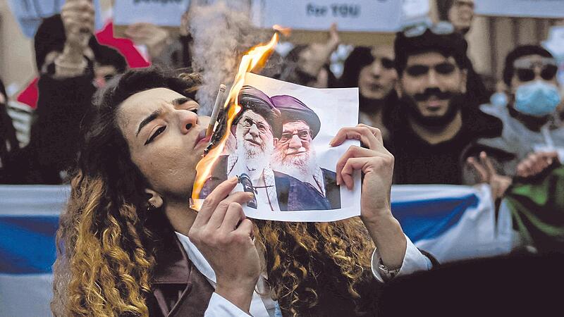 Eine Demonstrantin z&uuml;ndet sich ihre Zigarette an einem brennenden Foto des Obersten F&uuml;hrers des Iran, Ali Chamenei, an.