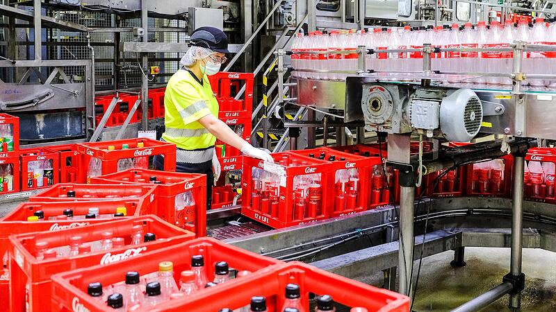 In einer endlosen Schlange ziehen K&auml;sten und Flaschen an den Mitarbeitern im Cola-Werk vorbei.