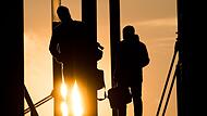 Zwei M&auml;nner gehen mit Aktentasche bei Sonnenaufgang &uuml;ber Br&uuml;cke