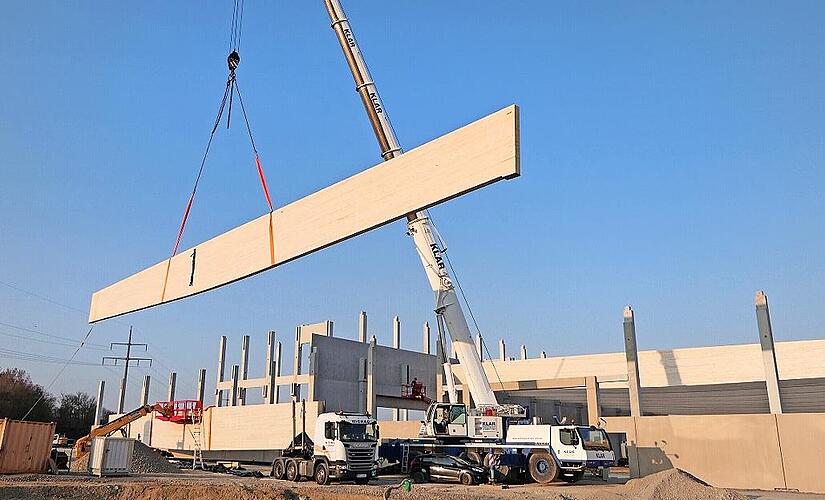 Mit einem Autokran werden die rund zw&ouml;lf Tonnen schweren Holzleimbinder in Ha&szlig;furt an ihren Bestimmungsort im Hallenneubau gehoben.
