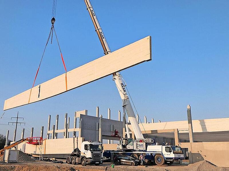 Mit einem Autokran werden die rund zw&ouml;lf Tonnen schweren Holzleimbinder in Ha&szlig;furt an ihren Bestimmungsort im Hallenneubau gehoben.