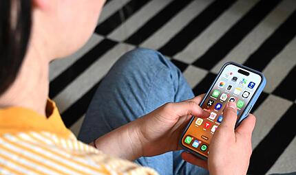 Eine Jugendliche blickt auf das Display ihres Smartphones, auf dem verschiedene Apps zu sehen sind.