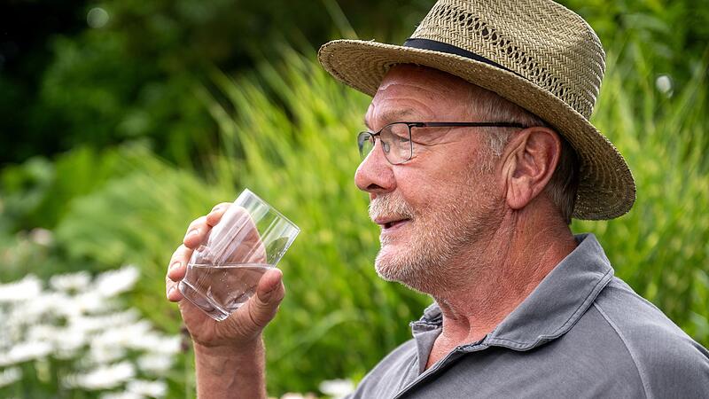 Ein Senior trinkt ein Glas Wasser im Sommer